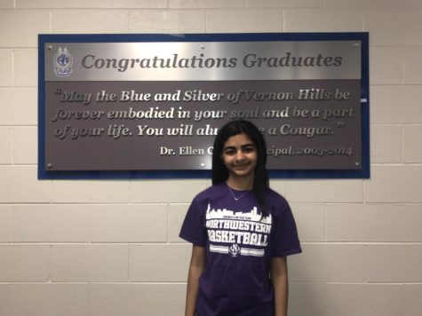 Rhea smiles in a Northwestern tshirt in front of the graduate sign.