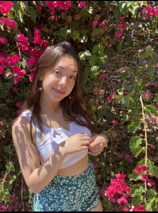 Alina is standing by a bush of flowers.
