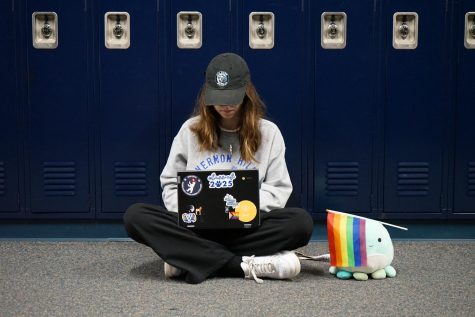 Abi Karl sits in the hallway next to a stuffed animal holding a pride flag.