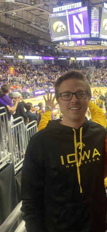 Neal Haussmann stands in from of the University of Iowa vs. Northwestern University basketball game scoreboard in an Iowa hoodie.