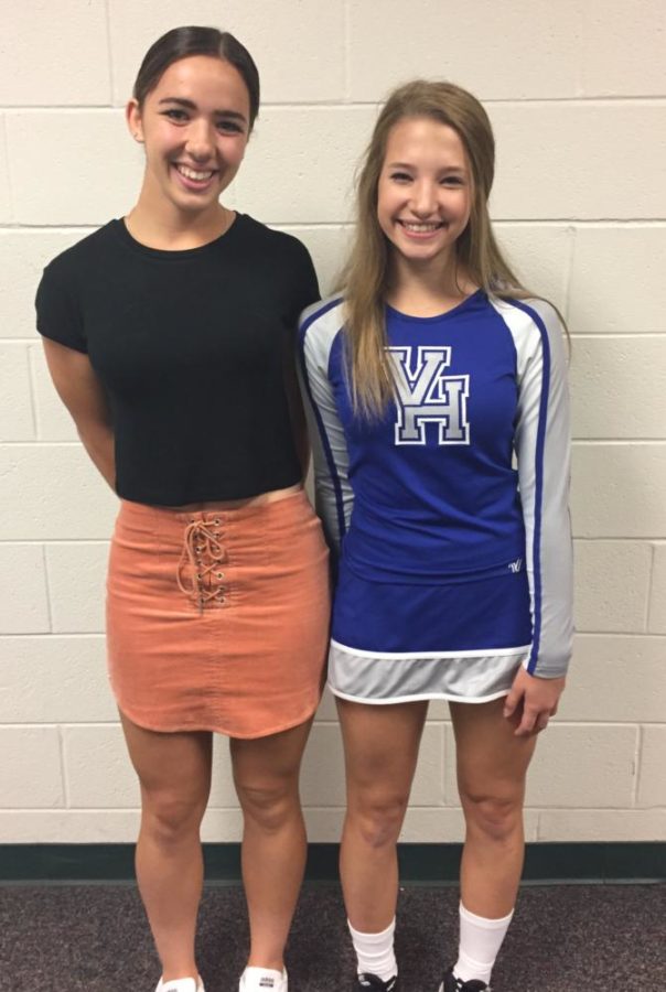 This image shows two students standing side by side. The student on the left wears a black t-shirt and orange skirt. The student on the right wears a Vernon Hills High School cheer uniform. The cheer uniforms skirt is shorter than the other girls orange skirt.
