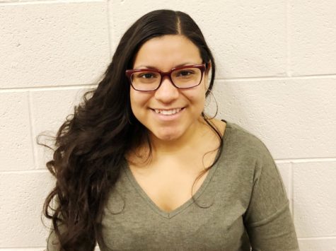 Angie Campos smiles in a green shirt in front of a white wall.