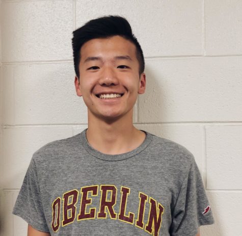 Ryan Kim smiles in an Oberlin shirt in front of a white wall.