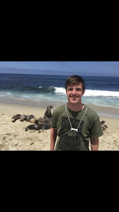 Picture of Carter Sherwin standing on a beach in front of the ocean and a pod of seals