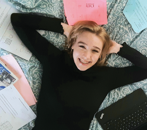 This is a photo of Katelyn on her bed surrounded by school work.