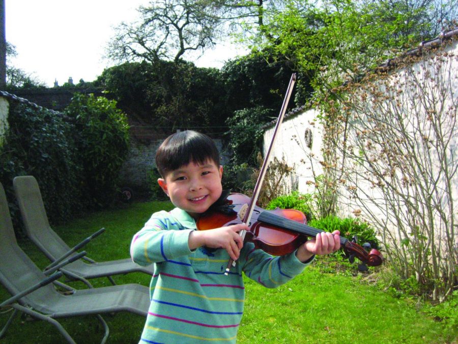This is a photo of Ian Joe playing the violin outside at a young age.