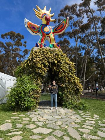 Senior Evan Kim stands in front of the Sun God statue at UCSD holding up a Triton symbol.