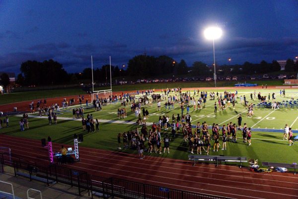 This is a photo of students on the football field at night under the lights at the kickoff dance. Students are standing around in groups.