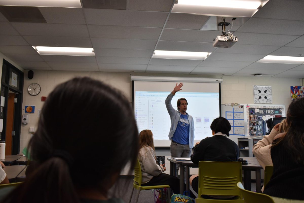 A student, left, watches as social studies teacher Brian Voss raises his hand while teaching the class.