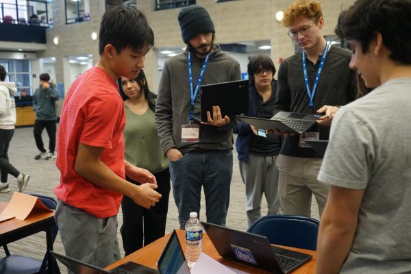 Luke Wu stands in front of a table, facing his computer to present his project to judges.