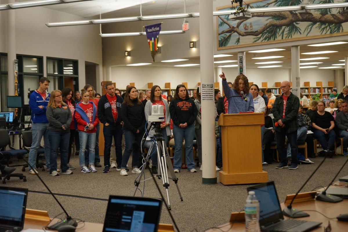 English teacher Amy Christian points to a frame of the D128 mission statement while addressing the Board of Education, with other teachers who live in the community standing behind her.